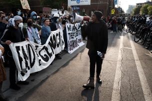 A protester with a megaphone walking on a street between a wall of protesters and another wall of police