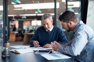 Male professor and student sit together at a table working on a paper