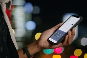 Cropped shot of a woman using a smartphone to order a cab in the city at night
