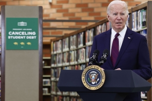 Joe Biden stands at a podium in front of bookshelves and a green sign that says Canceling Student Debt