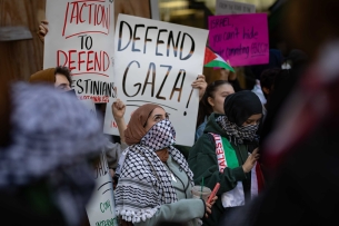 Hunter College students protest. A white sign with black letters says “Defend Gaza”