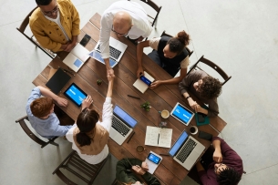 Aerial photo of a group of professional people gathered around a table with laptops and phones, some shaking hands.