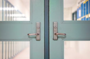 A picture of closed school doors with an empty hallway beyond.