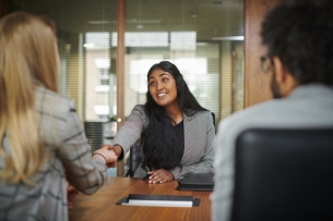 A student in business professional clothing shakes the hand of an individual