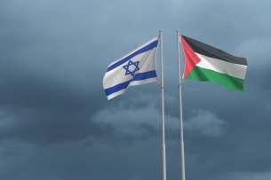 Israeli and Palestinian flags wave on two flagpoles next to one another.