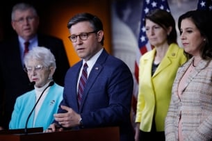 Mike Johnson, in a blue suit and flanked by several Republican leaders, stands at a podium