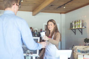 A young barista hands a man a coffee cup