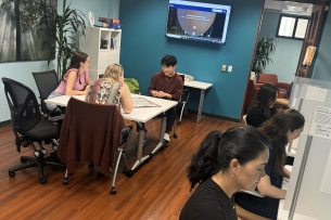 Students sit at computers and a group of students sits at a table together within the Kortschak Center for Learning and Creativity at USC.