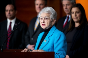 Virginia Foxx, in a bright blue blazer, stands behind a podium.