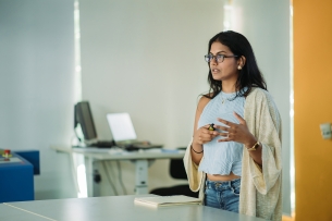 A young female student stands up in front of a classroom to give a presentation.