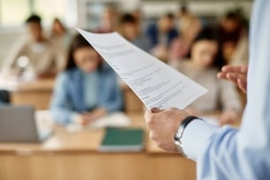 Close-up of university teacher reading a syllabus to a classroom of students.