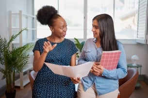 Two women discuss work solutions in an office, mentorship learning 