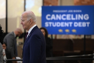 President Biden stands in front of a blurred-out blue sign that says "canceling student debt."