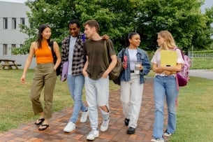 A group of diverse students carrying backpacks and books walk on a college campus .