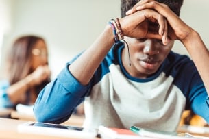 Depressed young African American student sitting in class with his head in his hands