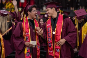 Two graduates of Victor Valley College smile and fist bump at graduation