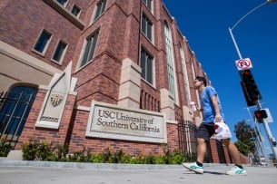 A student in a blue shirt walks past a brick campus building