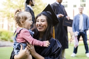 A young mother, in her cap and gown, smiles at her baby girl's silliness.