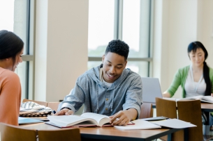 The young adult male receives tutoring in the library from a peer so he can better understand the material.