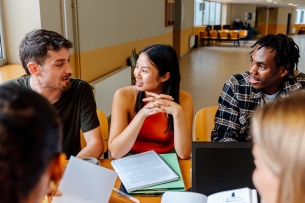 Multiracial group of students sitting at a university campus table studying together and chatting.