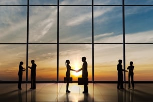 Three groups of two people stand before a large window looking out on the sun. They are shaking hands in greeting and talking together.