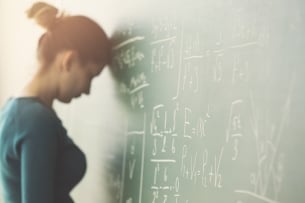 A student with her forehead against a chalkboard with math equations on it