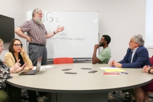 Mark Hoyert stands at a whiteboard with a group of five faculty members who are focused, considering his words