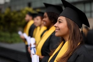 Students stand in a row in graduation caps and gowns. One student's profile is in focus, smiling. 