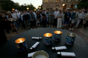 Candles and lighters are seen in the foreground while individuals stand in the background.