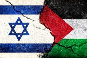 A photo illustration of two flags, one of Israel and the other of Palestine, colliding with each other with a crack going through both of them.