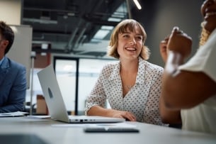 Three happy multiracial business people wearing businesswear smiling during discussion at meeting in office