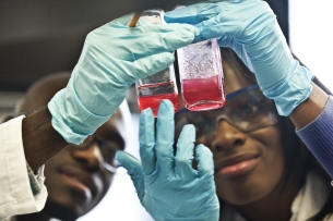 Two Howard University students hold beakers of red liquid.