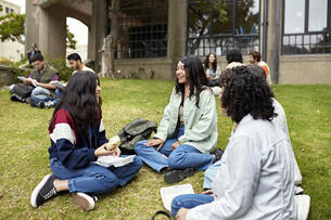 Focus on foreground group of women in teens and 20s sitting on grass and enjoying a break from classs