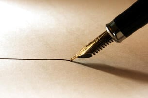 A close-up photo of a fountain pen with black ink being wielded to draw a thin line on paper.
