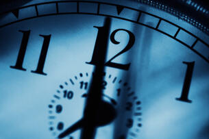 A close-up photo of a clock with a hand pointing to the 12.