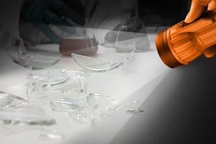 A flashlight shines a light on broken glass lab equipment.