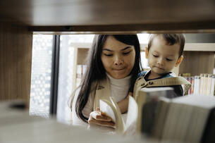 Young mother reading books to little son in library.