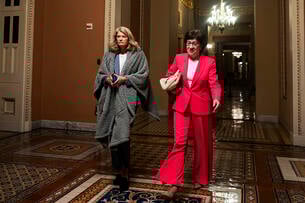 U.S. Sen. Lisa Murkowski (R-AK) and U.S. Sen. Susan Collins (R-ME) walk to the Senate floor during overnight votes at the U.S. Capitol. Murkowski has a blanket wrapped around her shoulders and Collins is wearing a red suit.