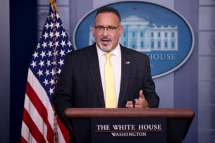 Secretary of Education Miguel Cardona, a middle-aged Hispanic man with a goatee wearing glasses and a business suit.