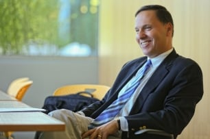 Ron Liebowitz sits in a chair in a navy suit, white shirt and blue striped tie