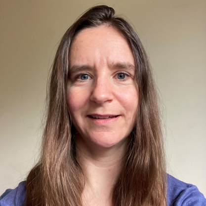 Anna Mills, a light-skinned woman with long brown hair, wearing a blue top