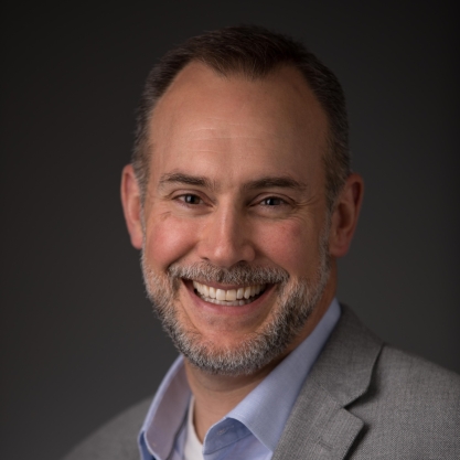 Steven Johnson, a light-skinned man with dark hair and a beard and mustache sprinkled with gray, wearing a gray jacket over a blue collared shirt and a white undershirt