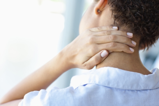 Close-up color photo of young woman rubbing her neck, shown from the back (face not shown)