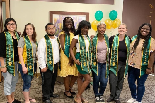 A group of graduates wearing green satin stoles denoting their participation in the Guardian Scholars Program.