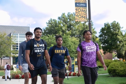 Four students, some in Coppin State University T-shirts, walk on campus. 