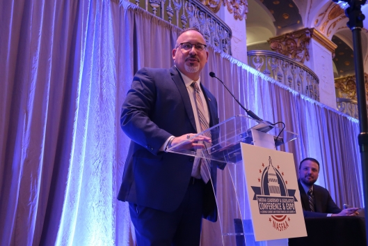 A Hispanic man in a suit at a podium