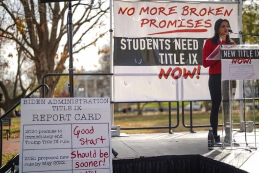 A student in a red sweater takes a podium at a Title IX protest in December