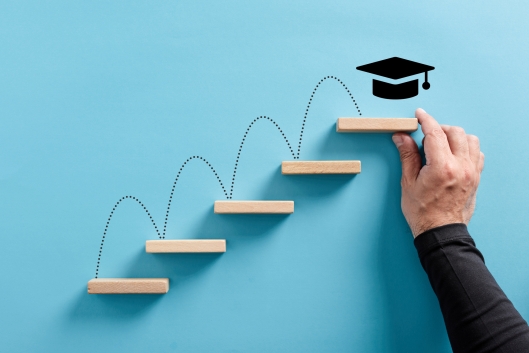 Male hand arranges a wooden block ladder with academic mortar board symbol at the top of the last step