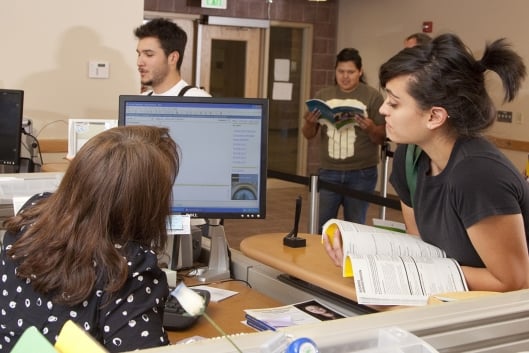 A student leans over a desk to look at a computer screen alongside a faculty member 