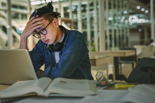 An overwhelmed student sitting in a library staring at his laptop 